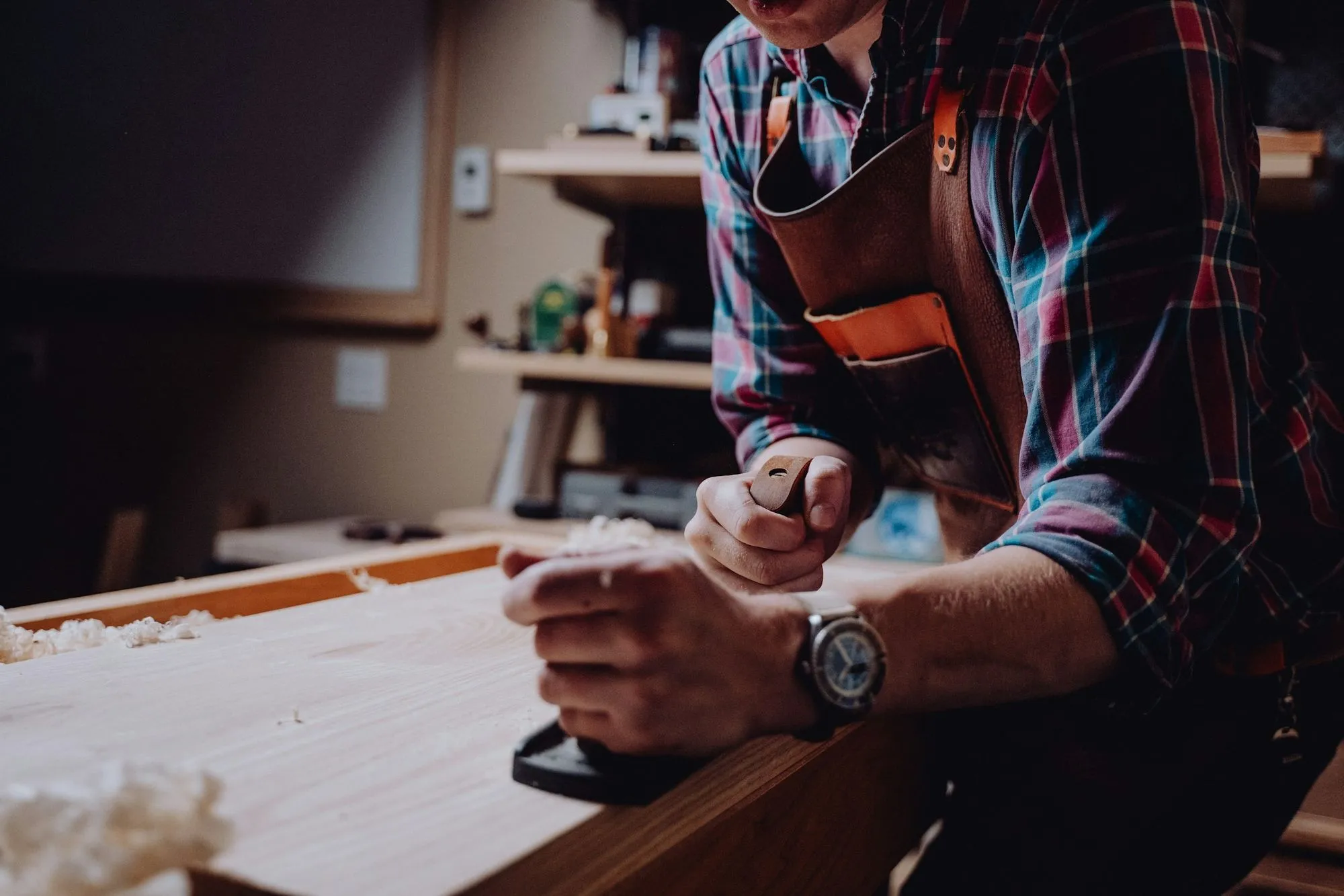 Carpenter in an apron planing the edge of a pale wood board at a workbench