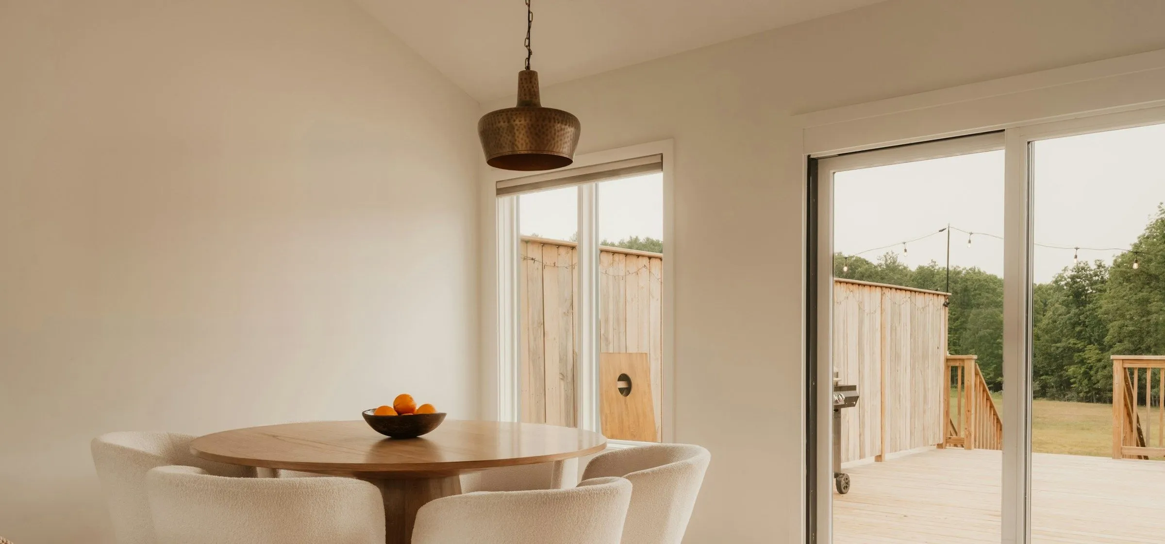 Garden room with a cream wall, a round oak table under a brass pendant and sliding doors to a new deck