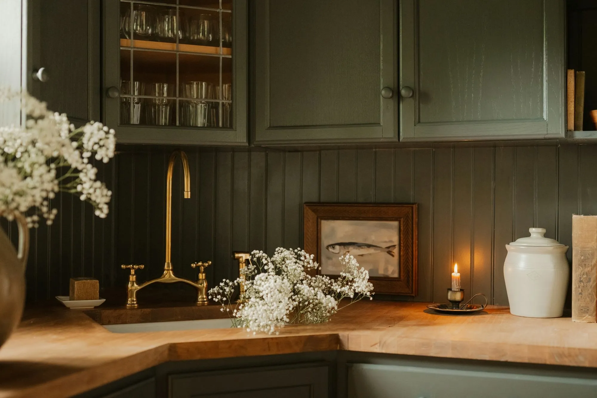 Green painted cabinets, a butcher block counter and an unlacquered brass bridge faucet