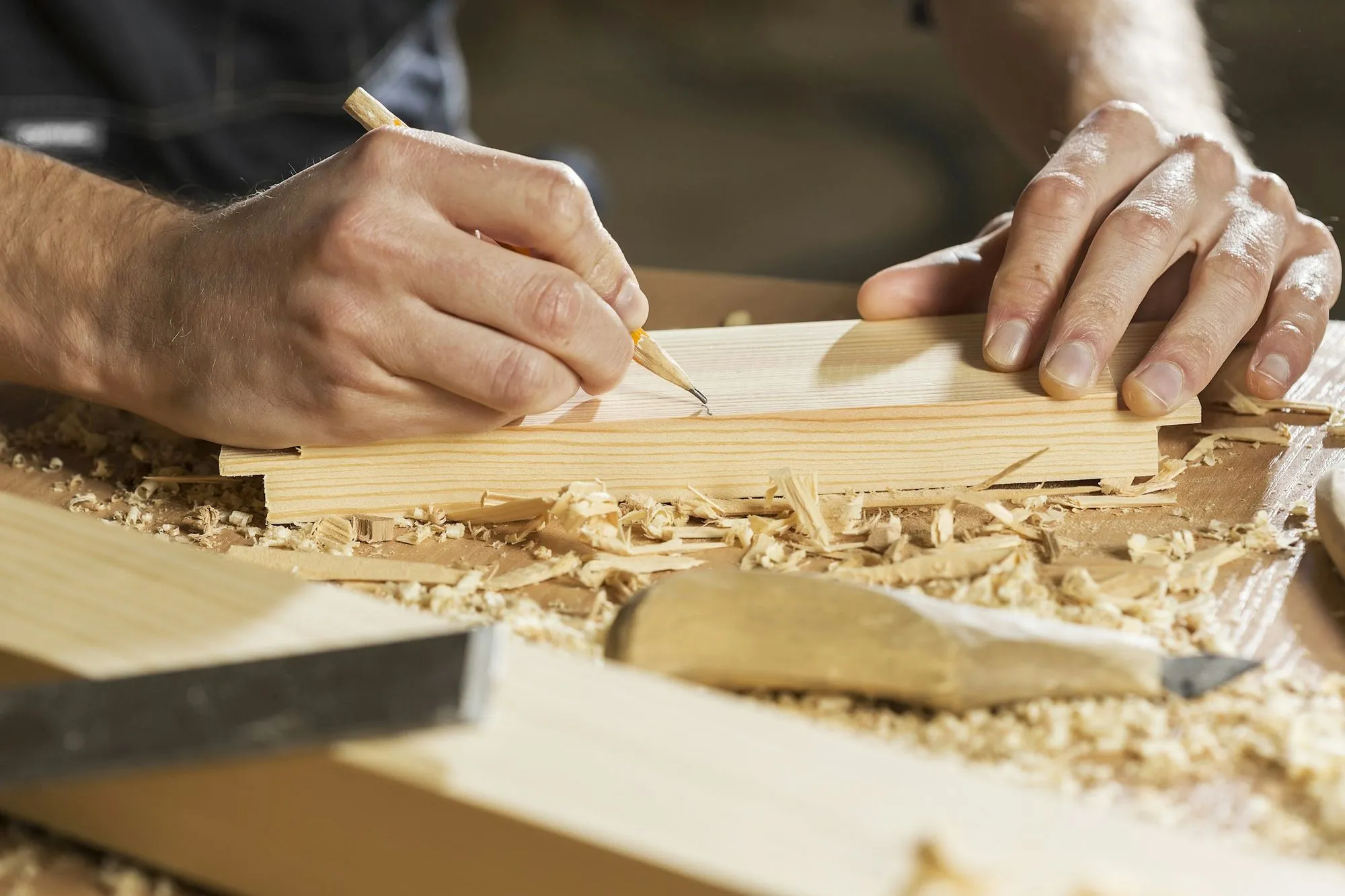 Hands marking a cut line on a pine board covered in fresh shavings