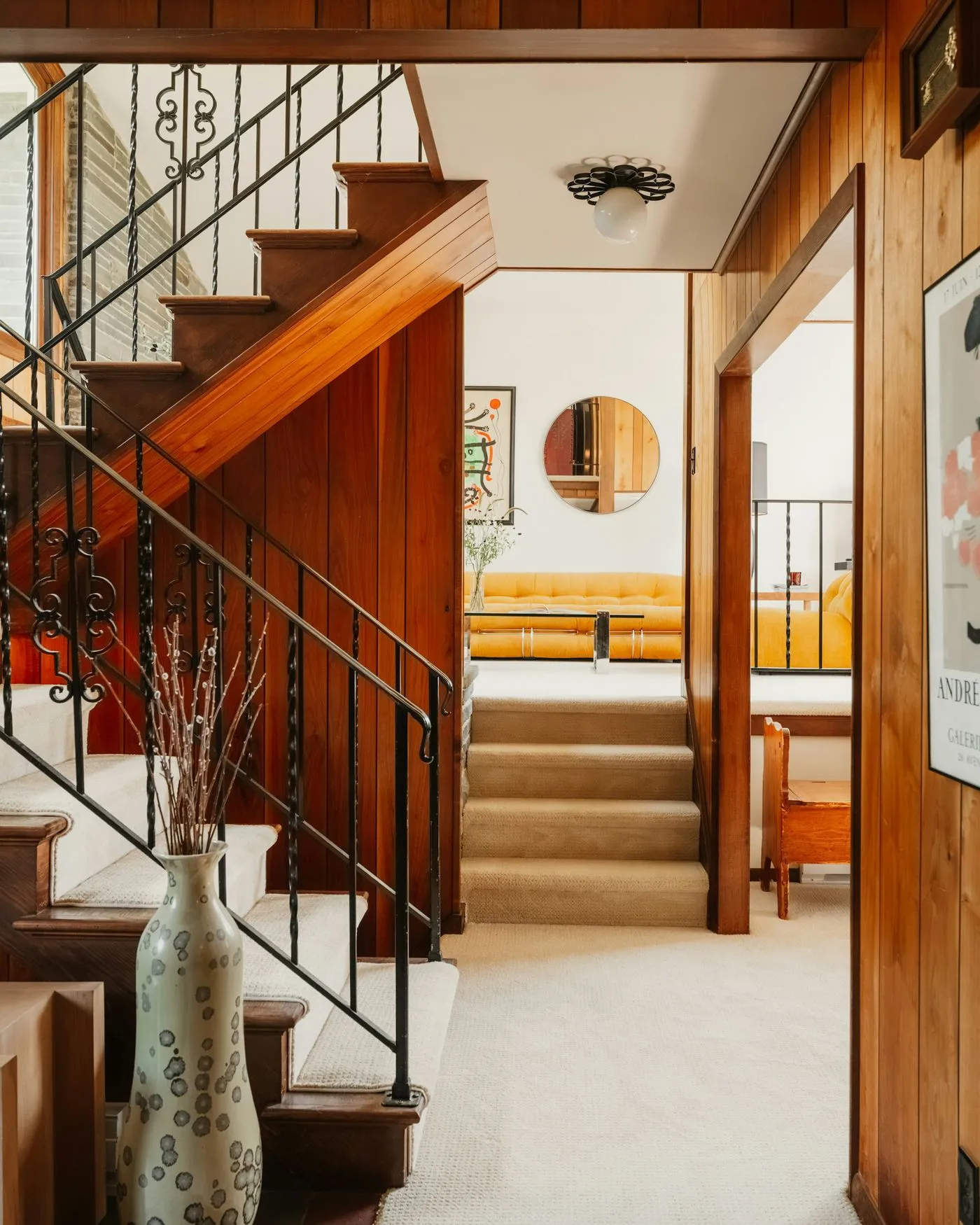 Split-level stair with wood treads and black iron railings between paneled walls