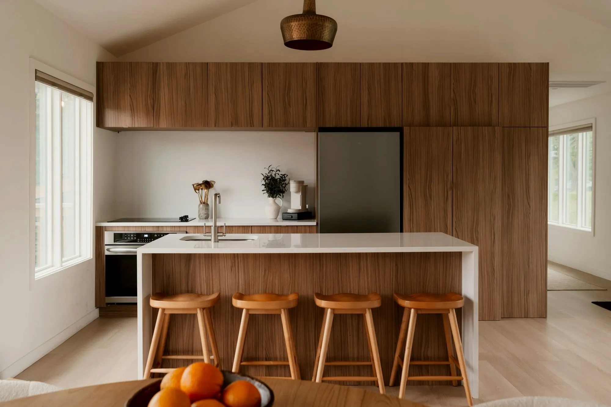 White island with four oak stools in front of floor-to-ceiling walnut cabinets and a brass pendant