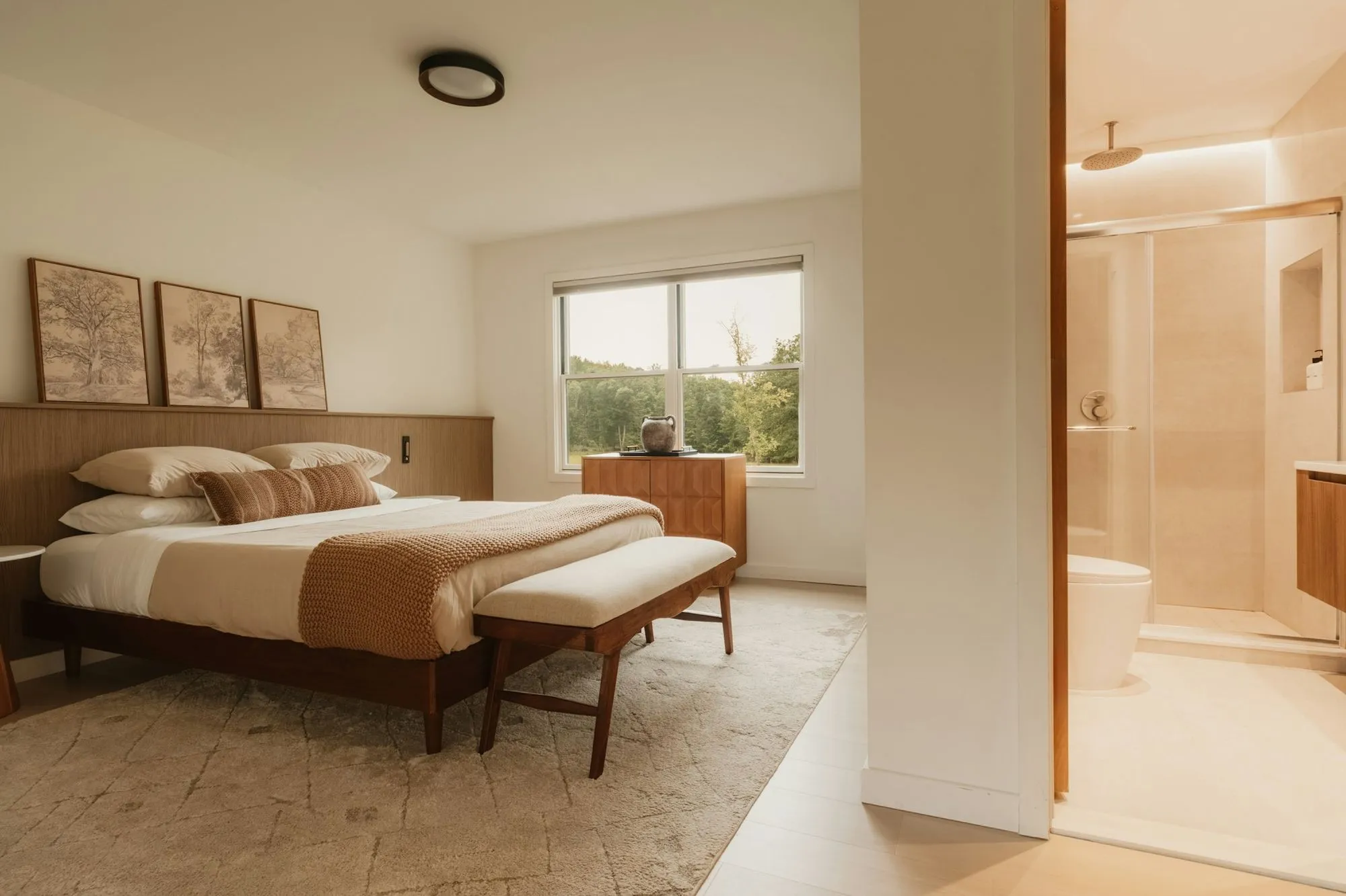 Bedroom with a walnut bed and bench, opening to a bath with a glass shower